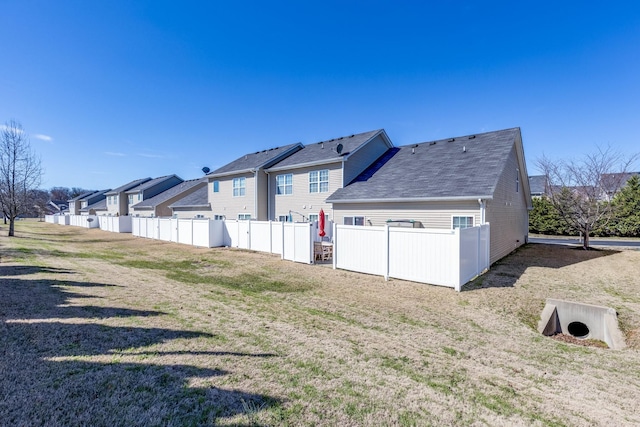 back of house featuring a residential view, roof with shingles, fence, and a lawn