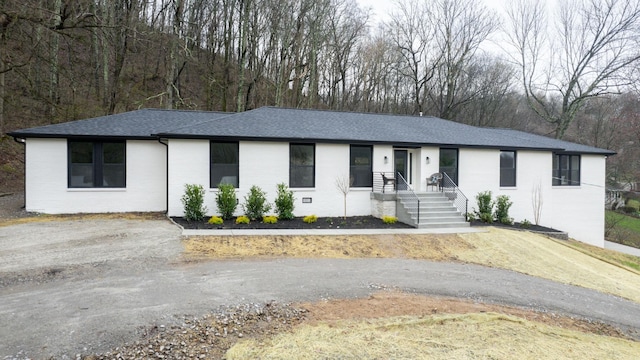 view of front of house featuring a shingled roof, crawl space, brick siding, and aphalt driveway