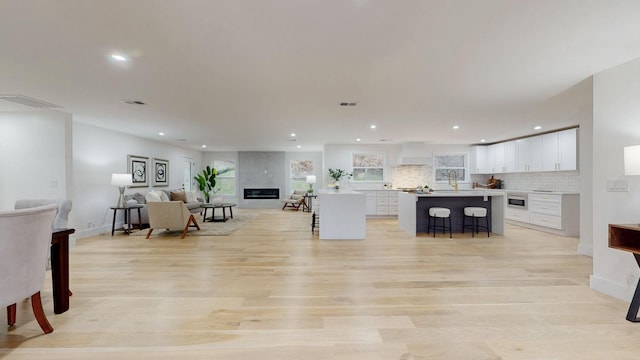 kitchen with a center island, a breakfast bar area, custom range hood, open floor plan, and white cabinetry