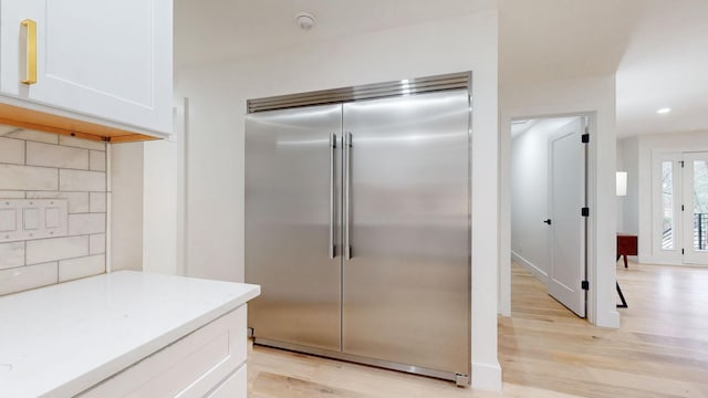 kitchen featuring tasteful backsplash, light countertops, light wood-style flooring, white cabinetry, and stainless steel built in refrigerator