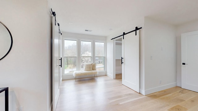 interior space with a barn door, visible vents, baseboards, and light wood-style flooring