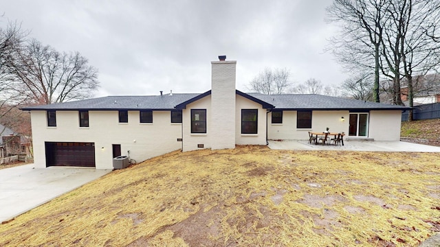 rear view of house with a patio, a chimney, concrete driveway, an attached garage, and central AC