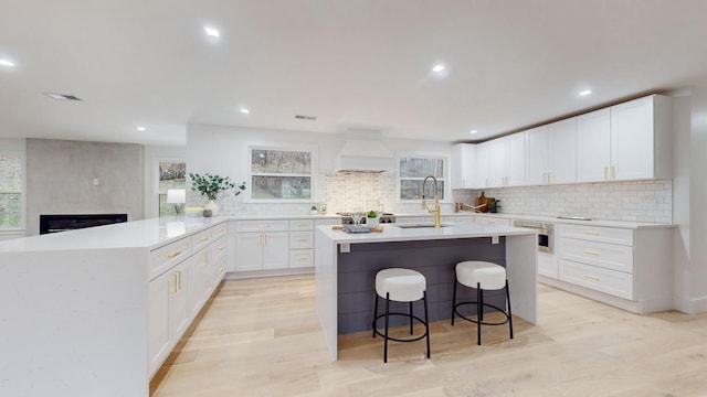 kitchen featuring custom exhaust hood, light countertops, light wood-style flooring, a sink, and a peninsula