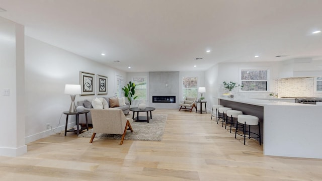 living room featuring a large fireplace, baseboards, light wood-style flooring, and recessed lighting