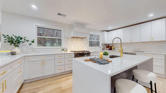 kitchen featuring a breakfast bar area, stainless steel stove, premium range hood, light wood-style floors, and light countertops