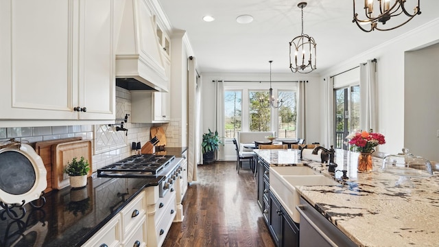 kitchen with light stone counters, a notable chandelier, crown molding, white cabinetry, and a sink