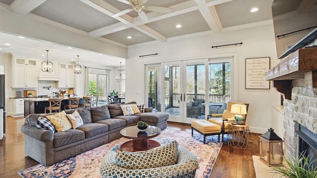 living area featuring beam ceiling, a fireplace, wood finished floors, coffered ceiling, and baseboards