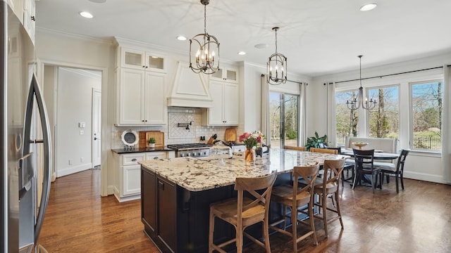 kitchen with custom exhaust hood, freestanding refrigerator, decorative backsplash, dark wood-style floors, and an inviting chandelier