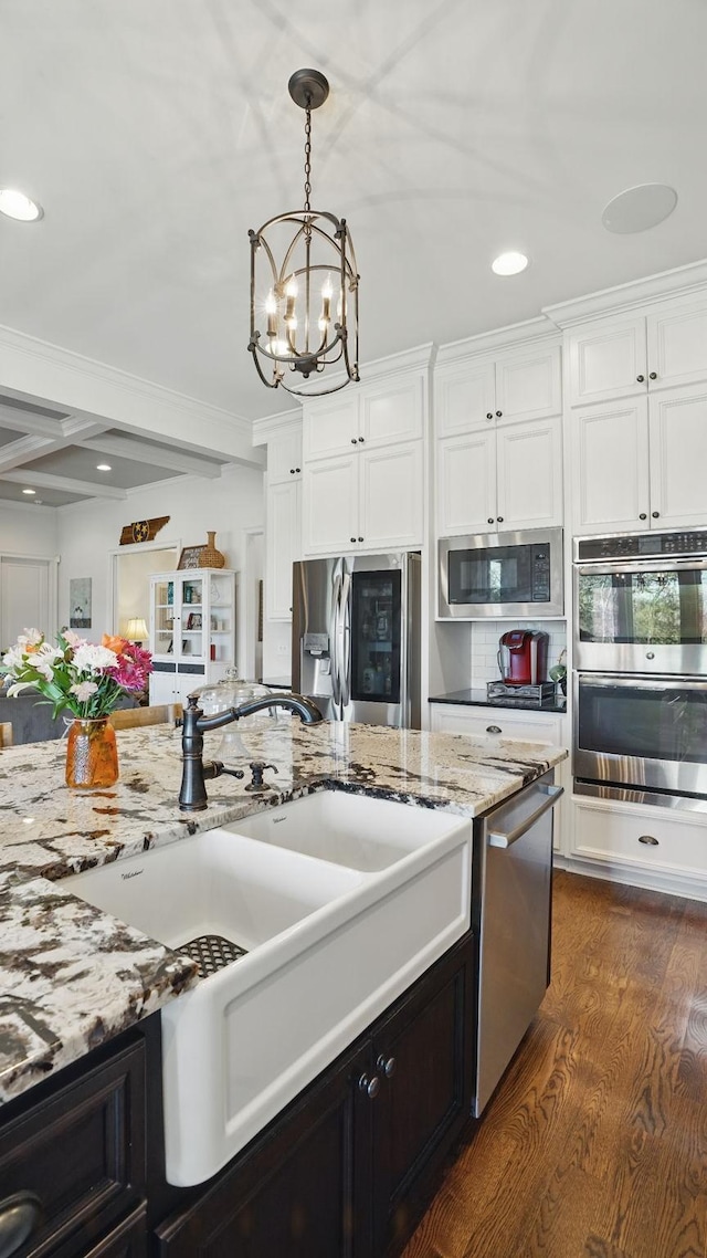 kitchen featuring white cabinets, dark wood-style floors, appliances with stainless steel finishes, crown molding, and a sink