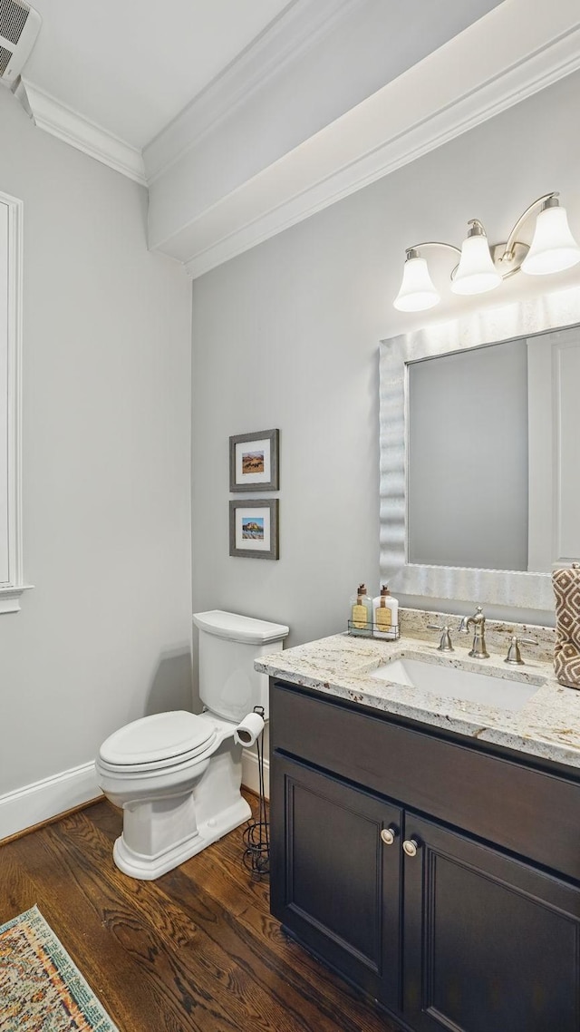 bathroom with toilet, wood finished floors, vanity, baseboards, and crown molding