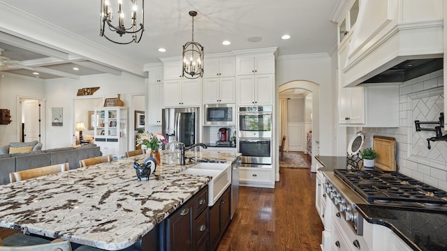 kitchen with arched walkways, beam ceiling, stainless steel appliances, a sink, and premium range hood