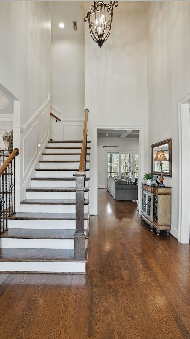 foyer with stairway, wood finished floors, a high ceiling, crown molding, and a chandelier