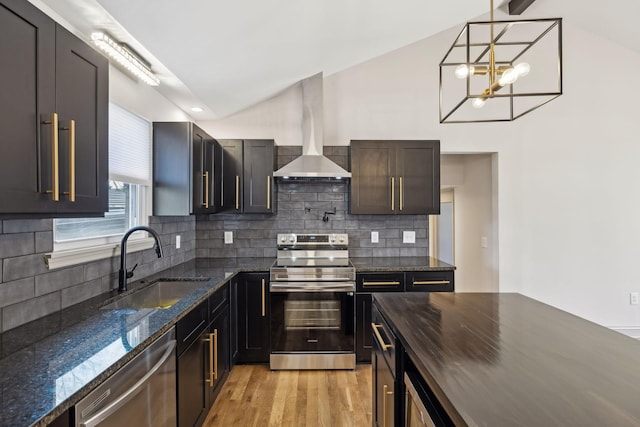 kitchen with appliances with stainless steel finishes, light wood-style floors, vaulted ceiling, a sink, and wall chimney range hood