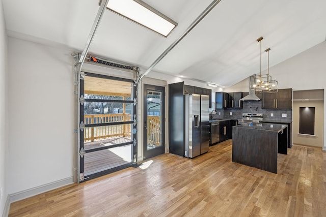 kitchen featuring appliances with stainless steel finishes, backsplash, a center island, light wood finished floors, and dark countertops