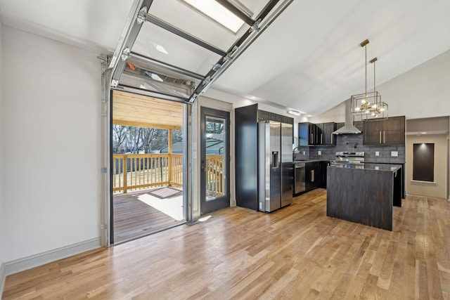 kitchen with wall chimney exhaust hood, appliances with stainless steel finishes, a sink, light wood-type flooring, and backsplash