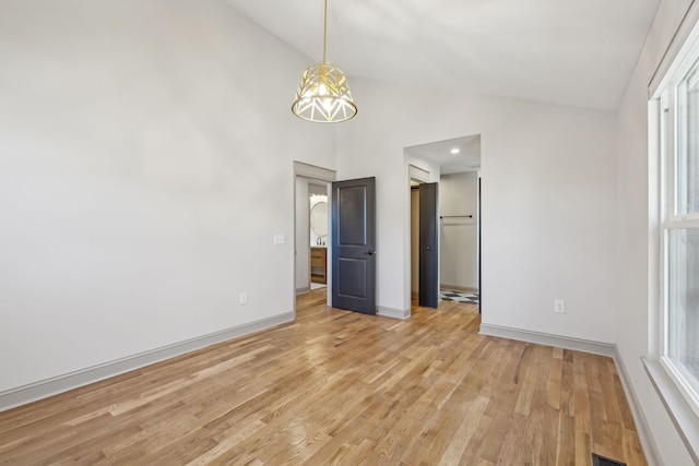 empty room featuring light wood finished floors, baseboards, visible vents, and high vaulted ceiling