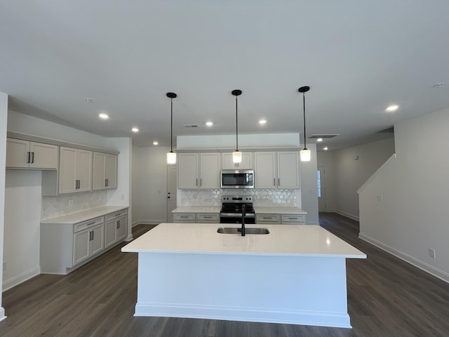 kitchen featuring a kitchen island with sink, appliances with stainless steel finishes, dark wood finished floors, and a sink