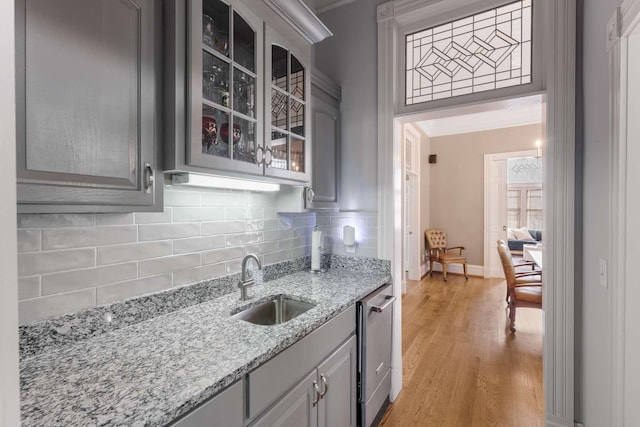 kitchen with decorative backsplash, dishwasher, gray cabinetry, light wood-style floors, and a sink