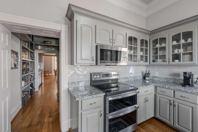 kitchen featuring stainless steel appliances, dark wood-style flooring, gray cabinets, glass insert cabinets, and crown molding