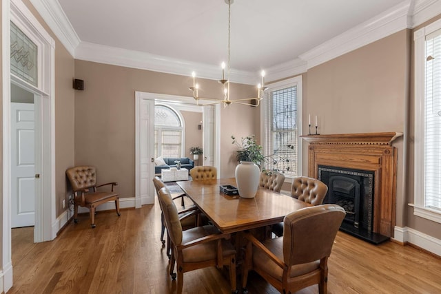 dining space with a fireplace with raised hearth, ornamental molding, light wood-style flooring, and baseboards