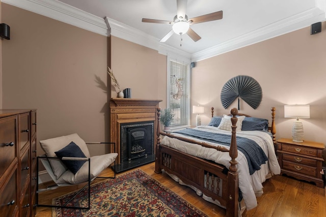 bedroom featuring ceiling fan, a fireplace, crown molding, and wood finished floors