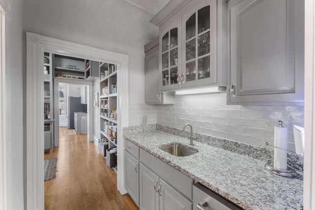 kitchen with light stone counters, tasteful backsplash, glass insert cabinets, a sink, and light wood-type flooring