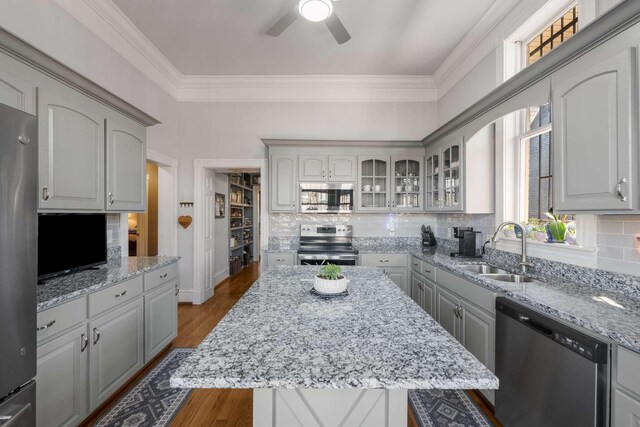 kitchen featuring stainless steel appliances, wood finished floors, a sink, glass insert cabinets, and crown molding