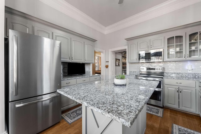 kitchen with light stone counters, stainless steel appliances, dark wood finished floors, glass insert cabinets, and crown molding