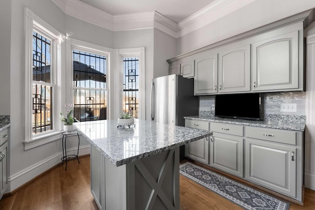 kitchen featuring a center island, baseboards, ornamental molding, decorative backsplash, and dark wood finished floors