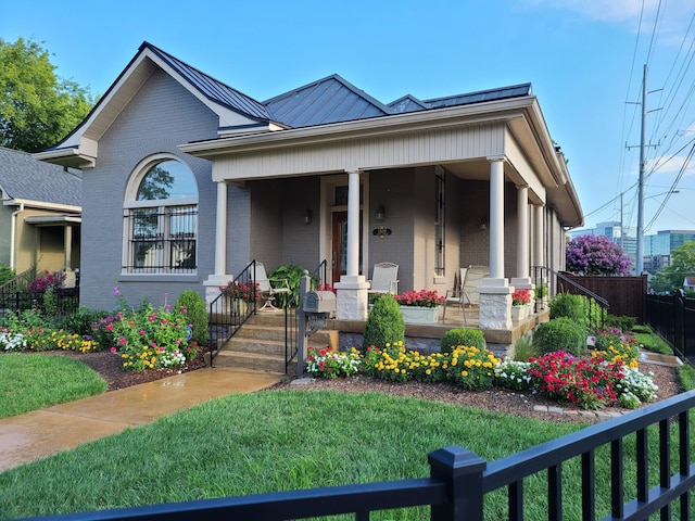 view of front of home with brick siding, covered porch, a standing seam roof, metal roof, and fence