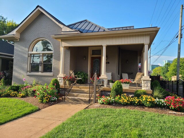 view of front facade featuring metal roof, a standing seam roof, fence, a porch, and brick siding