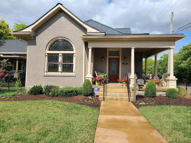 view of front of home with a porch, brick siding, fence, a standing seam roof, and a front yard