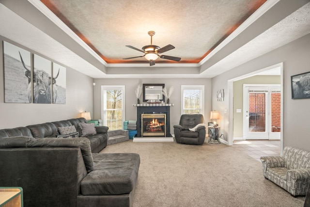 carpeted living area with a glass covered fireplace, a raised ceiling, and a wealth of natural light