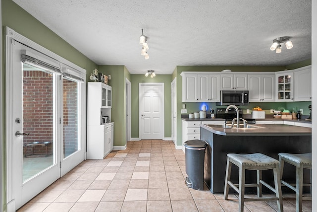 kitchen featuring light tile patterned floors, electric range, stainless steel microwave, a kitchen breakfast bar, and a sink