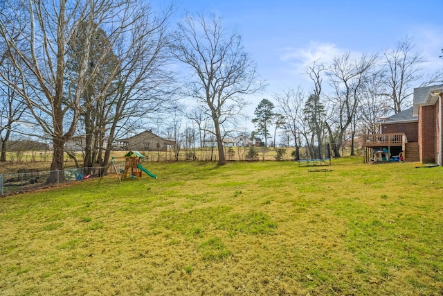 view of yard featuring a trampoline, a playground, a deck, a fenced backyard, and stairs