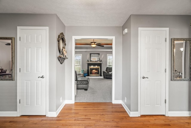 corridor with light wood-type flooring, a textured ceiling, and baseboards