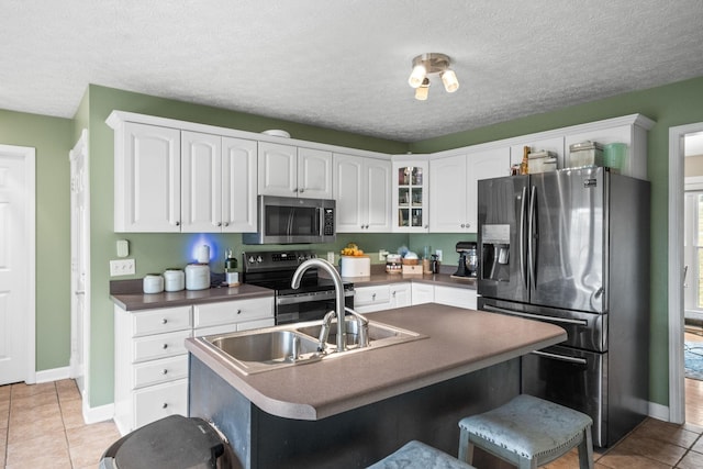 kitchen with dark countertops, appliances with stainless steel finishes, a kitchen breakfast bar, glass insert cabinets, and white cabinetry