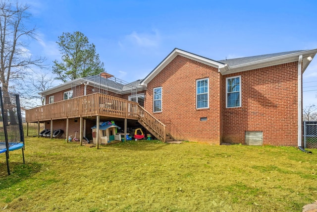 rear view of property with a yard, a trampoline, a deck, and brick siding