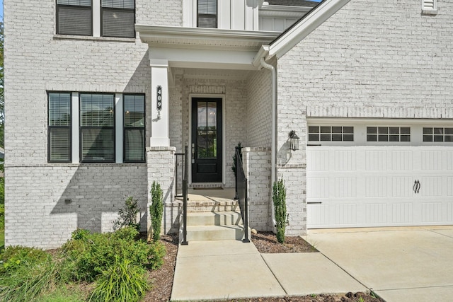 view of exterior entry with driveway, brick siding, board and batten siding, and an attached garage