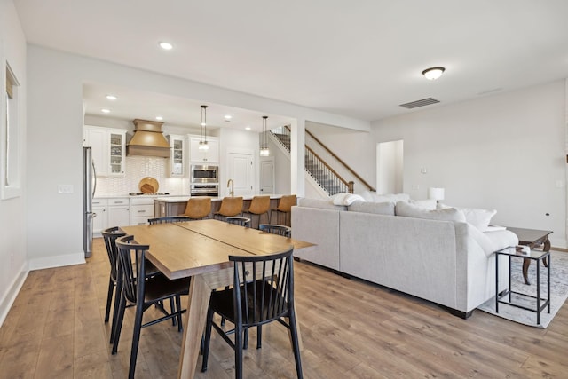 dining space with light wood-style flooring, stairway, visible vents, and baseboards