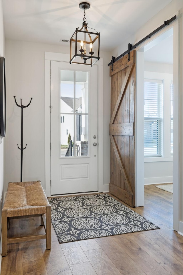 doorway to outside with a barn door, a notable chandelier, wood finished floors, visible vents, and baseboards