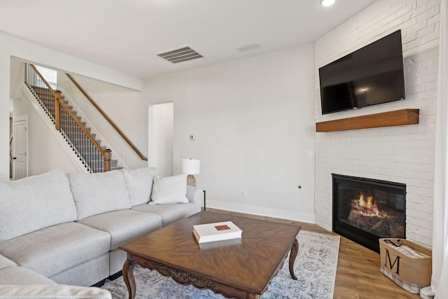 living room featuring a fireplace, visible vents, stairway, wood finished floors, and baseboards