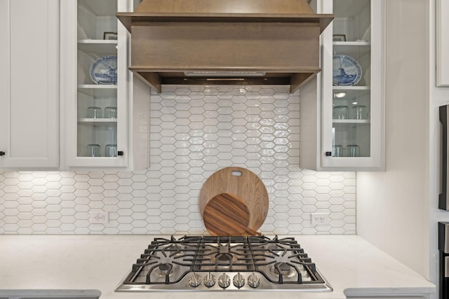 kitchen featuring glass insert cabinets, backsplash, white cabinets, and stainless steel gas stovetop