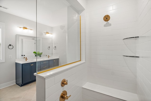 bathroom with double vanity, visible vents, tiled shower, tile patterned flooring, and a sink