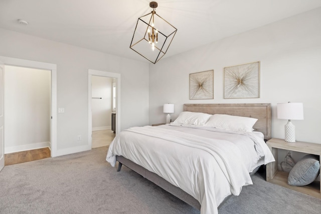 carpeted bedroom featuring an inviting chandelier, ensuite bath, and baseboards