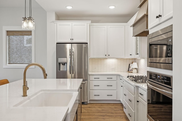 kitchen with light wood-style flooring, stainless steel appliances, a sink, white cabinetry, and decorative light fixtures