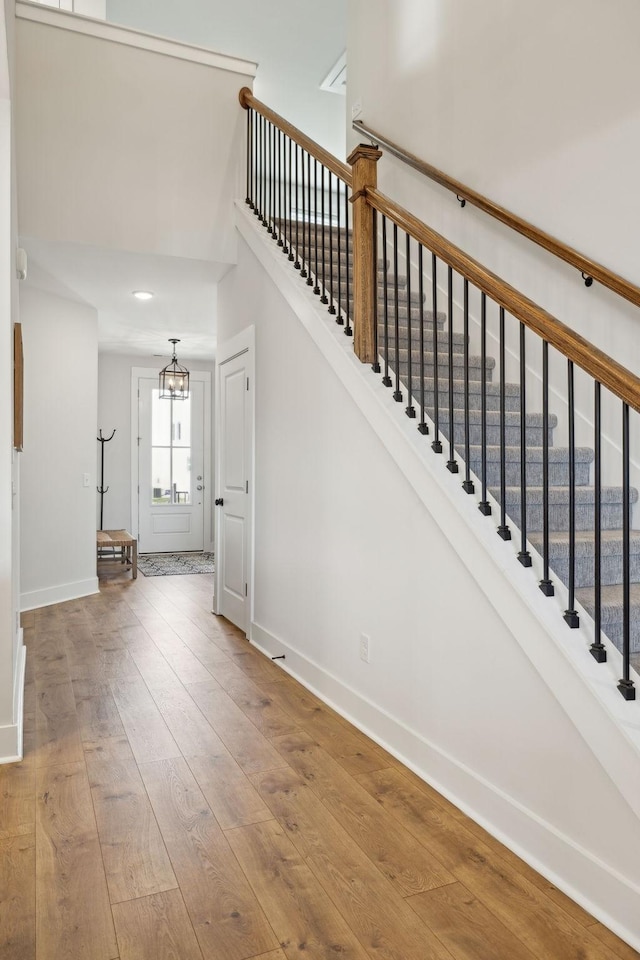 stairs with baseboards, a towering ceiling, hardwood / wood-style floors, and an inviting chandelier