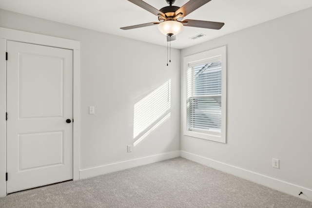 carpeted spare room with visible vents, baseboards, and a ceiling fan