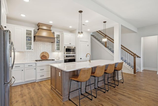 kitchen featuring stainless steel appliances, a breakfast bar, wood finished floors, and custom range hood