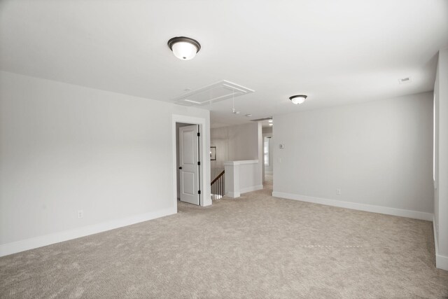 spare room with attic access, baseboards, and light colored carpet